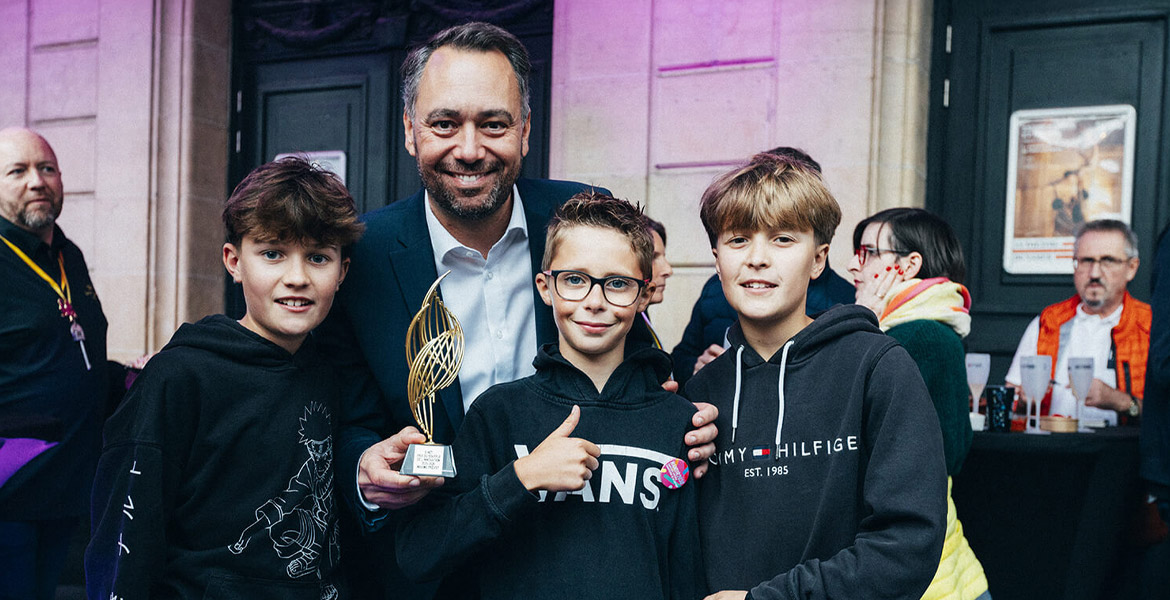 Maxime Prévot posant fièrement avec son trophée Souffle de l'Innovation, entouré de 3 enfants.