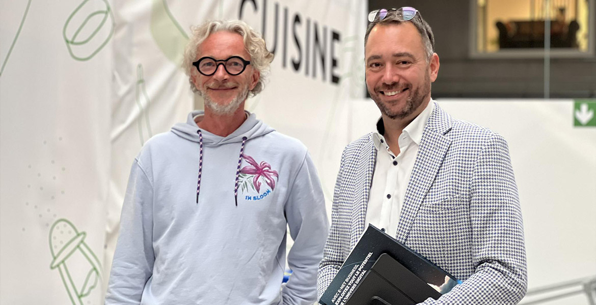 Maxime Prévot et le directeur d'Épicurus lors de l'inauguration de la formation dans les entrepôts de e-net, avec une affiche 'Cuisine' en arrière-plan.