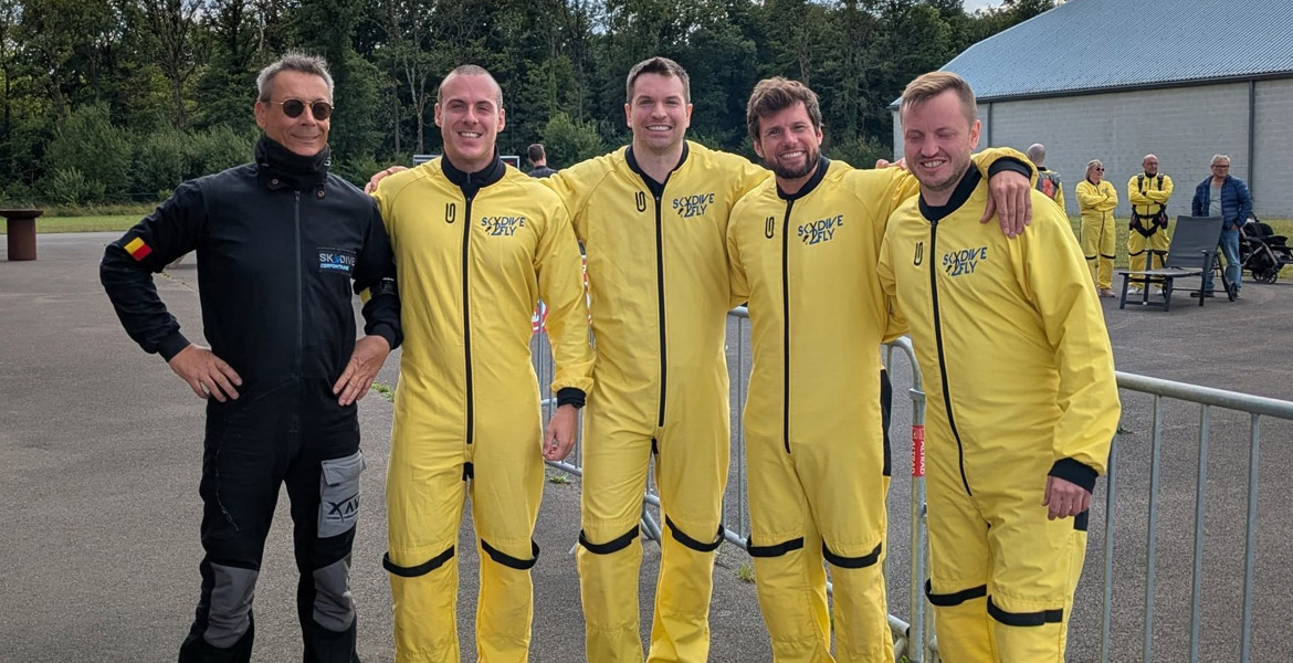 Paul Marien (à gauche) avec quatre clients de Skydive 2Fly, prêts à sauter en parachute, vêtus de combinaisons jaunes.